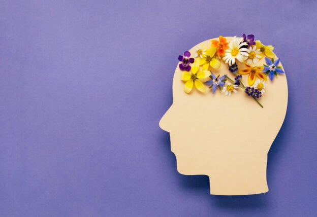 World mental health day concept. Human head symbol and flowers on a violet background.